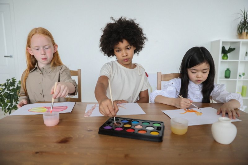 Drei Kinder malen Bilder mit Aquarellpinsel und Wasserfarben