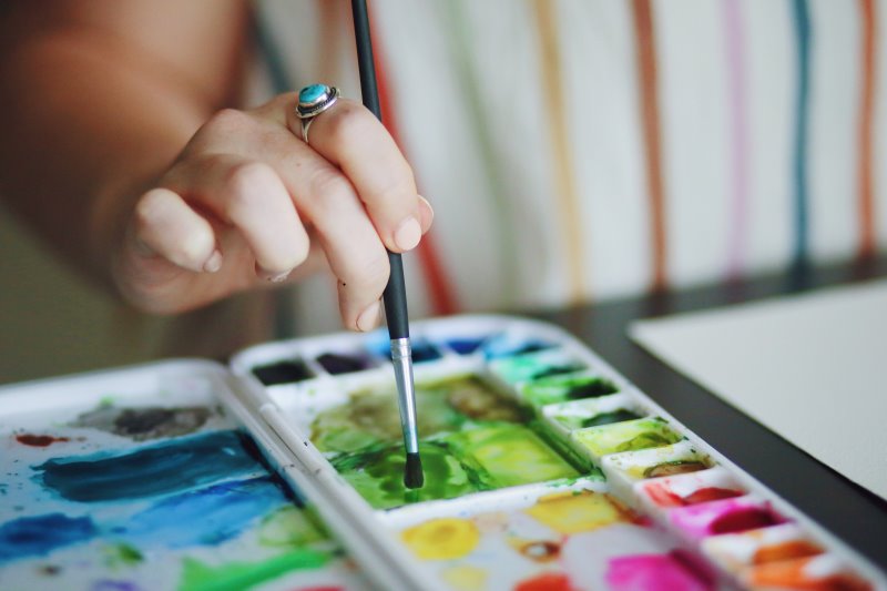Eine Person mischt Wasserfarbe mit einem Aquarellpinsel in einer Mischpalette. 